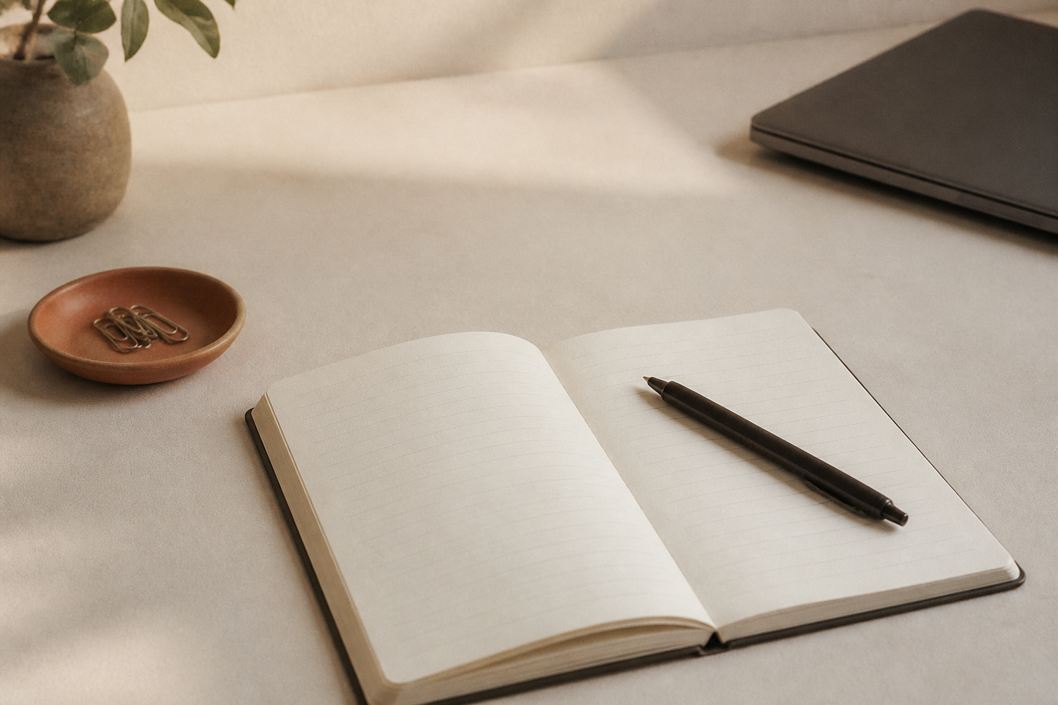 Open cream notebook with ink pen and terracotta dish of paperclips